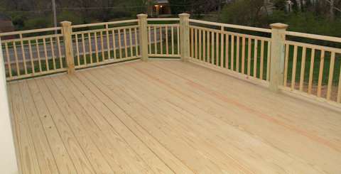 A wooden deck with light-colored planks and a railing overlooks a grassy area and a road—perfect inspiration for patio builders or anyone looking to transform their space with help from local landscaping companies.
