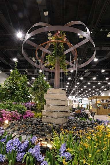 Indoor garden display with a circular metal structure, suspended plants, stacked stone centerpiece, and water feature—an inspiring showcase for landscaping companies seeking creative exhibition hall designs.