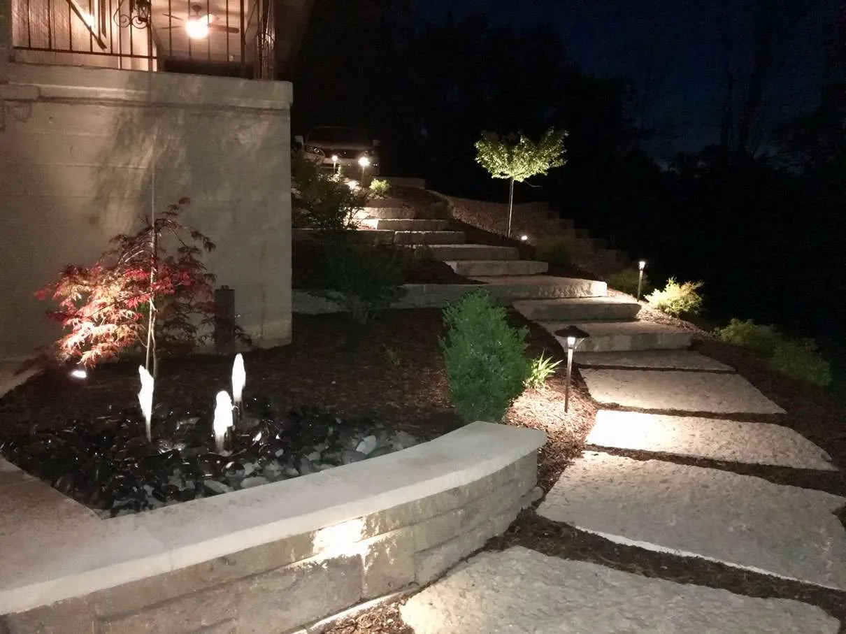 Illuminated stone garden steps with pathway lights and a small fountain at night.