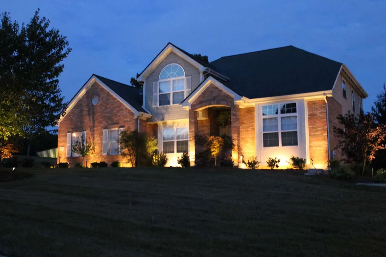 Two-story brick house with warm landscape lighting highlighting the front yard at dusk.