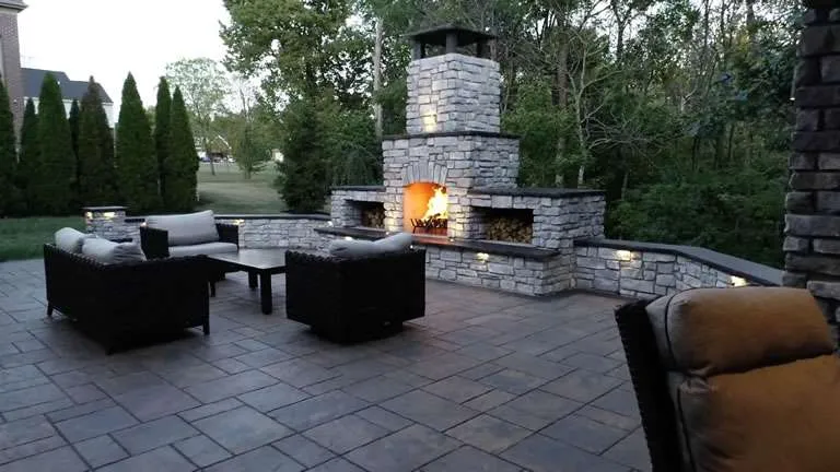 j Two-story brick house with warm landscape lighting highlighting the front yard at dusk.
